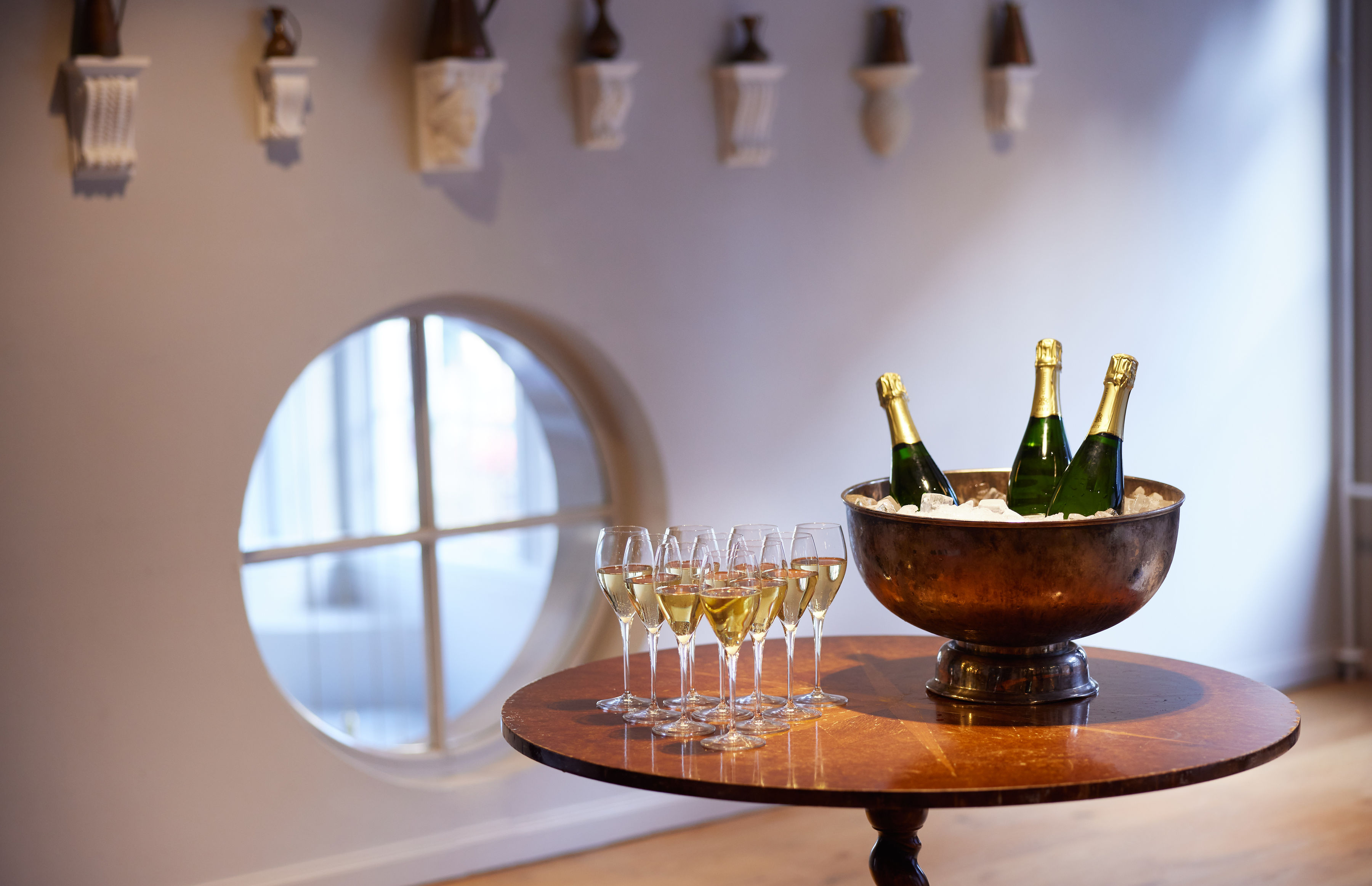 A table with champagne bottles in ice, surrounded by glasses ready for a toast, and a round window in the background.