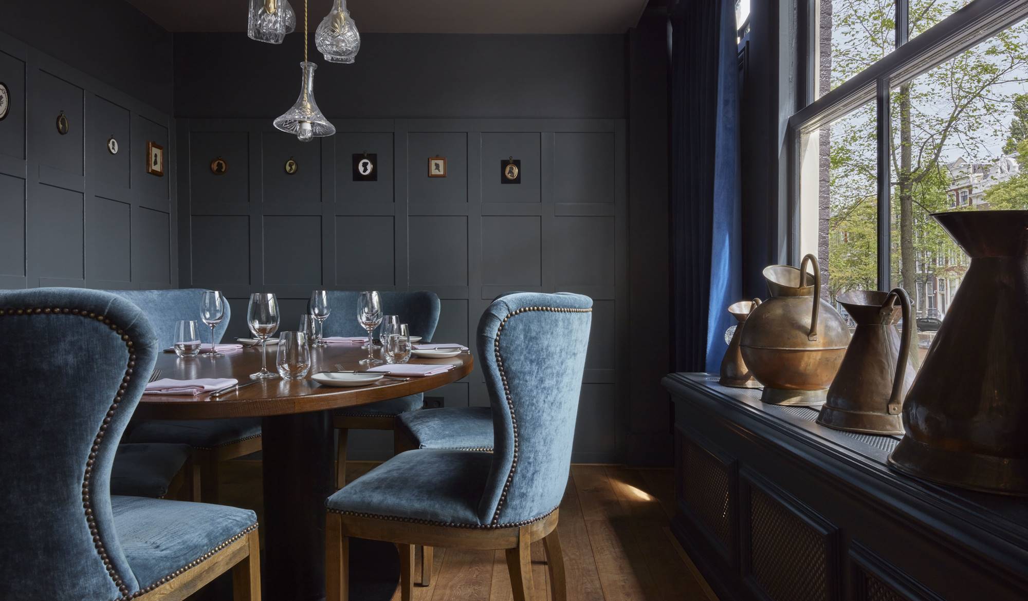 A semi-private dining room at Jansz. Amsterdam with a round table, blue velvet chairs, and pendant lights.