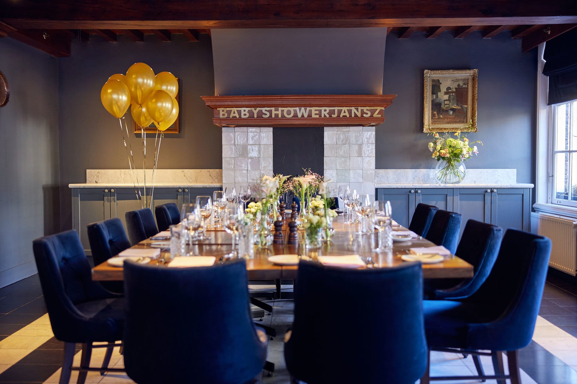 A long table set for a baby shower in Amsterdam with golden balloons and flower arrangements at restaurant Jansz.