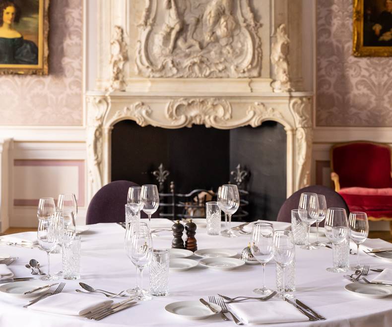 A formal dining table at a banquet at Pulitzer Amsterdam with crystal glassware and silver cutlery, with a marble fireplace.