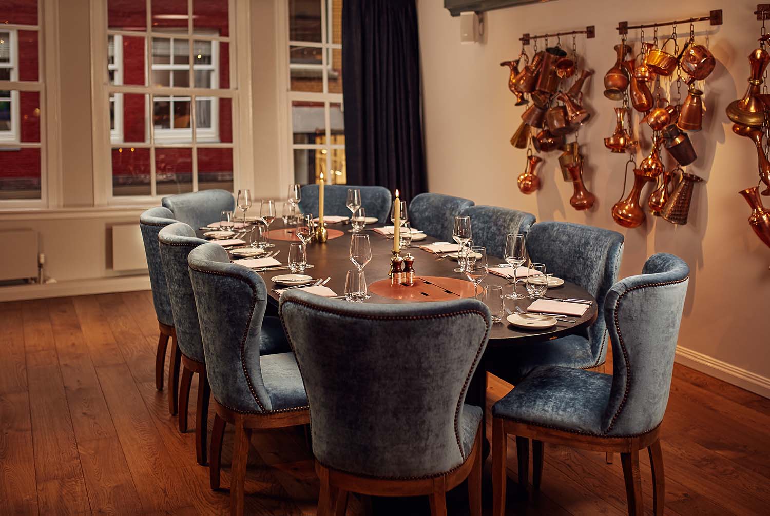 A large wooden dining table set for a private meal in Amsterdam at Jansz. with velvet chairs and copper pots on the wall.