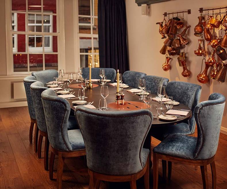 A large wooden dining table set for a private meal in Amsterdam at Jansz. with velvet chairs and copper pots on the wall.